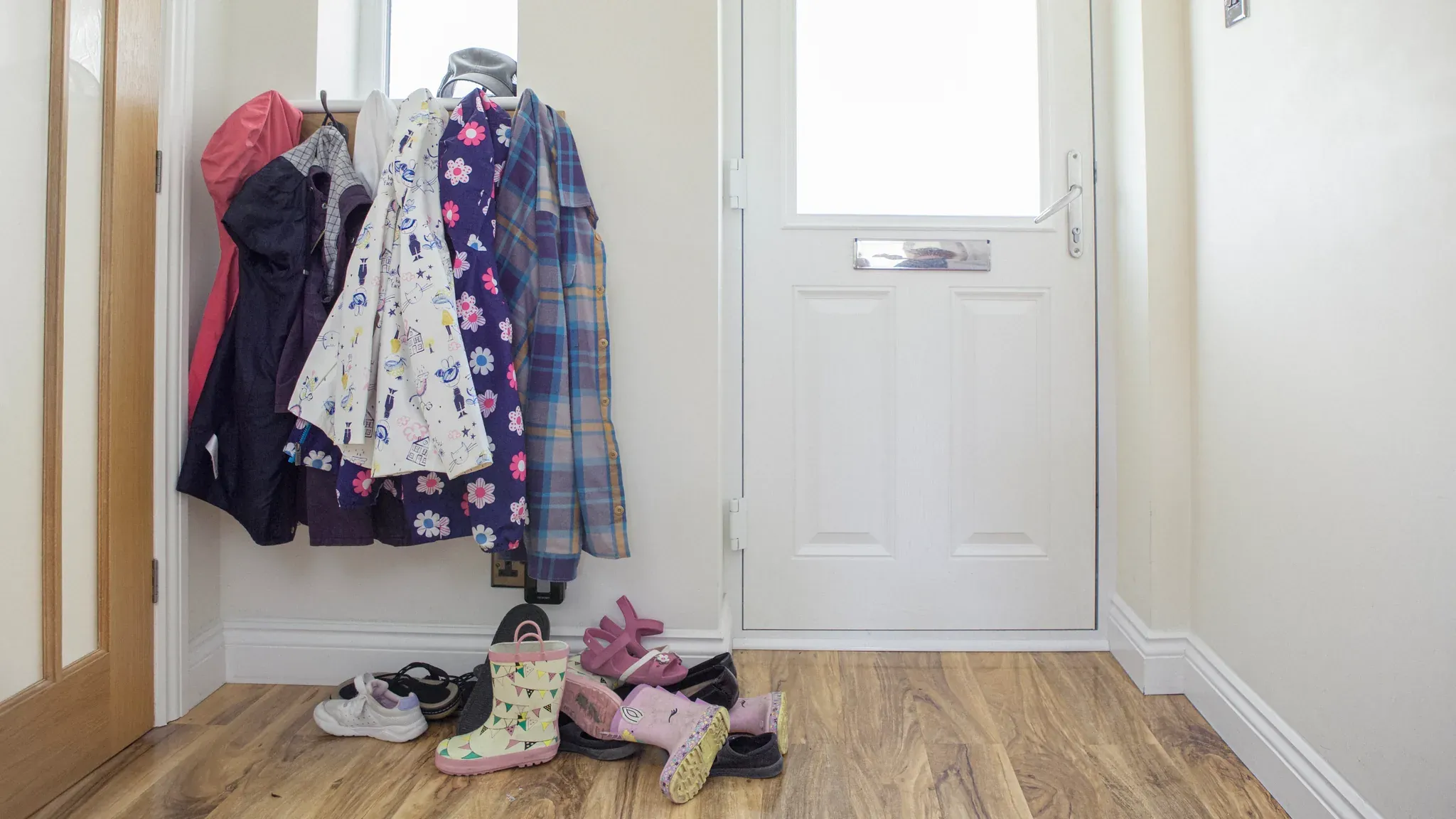 Coats on hooks and children's shoes by the front door of a family home