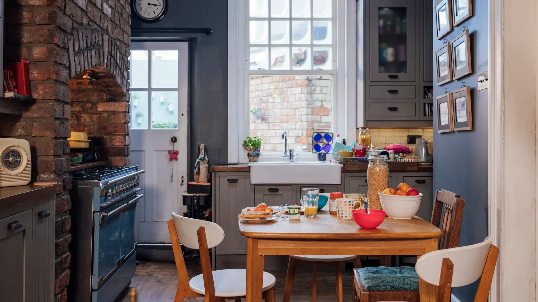 A kitchen table set for breakfast in a family kitchen, with a range cooker beside a brick chimney breast