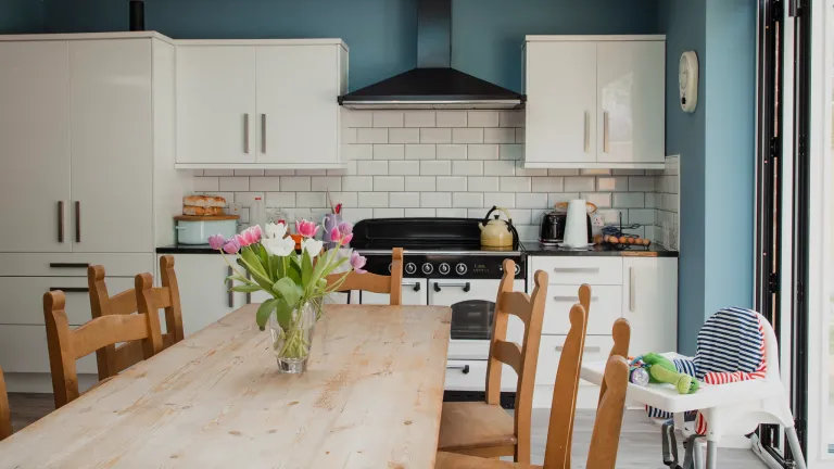 A long wooden dining table with a vase of tulips in a bright family kitchen