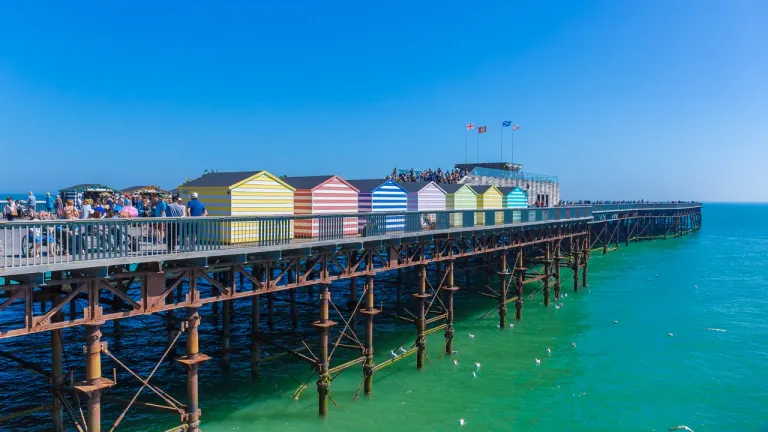 Colourful beach huts along the deck of Hastings Pier above a turquoise sea