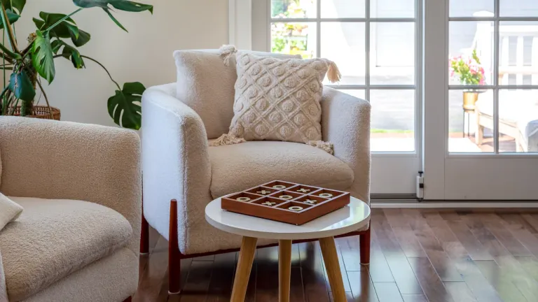 Two cream armchairs and a low table with a wooden board game in a bright sitting room